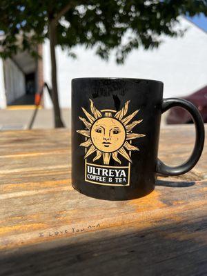 Ultreya mug on a picnic table that has "I love you ^_^" written in black ink.