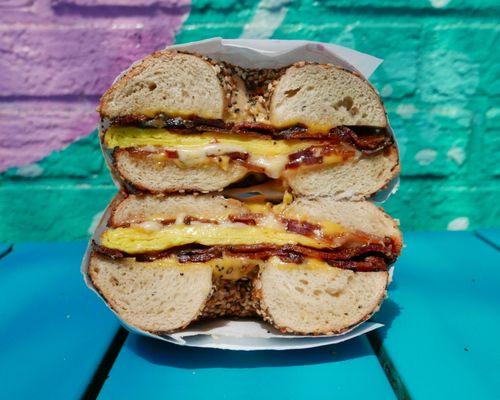 Our Bacon Sun City bagel sandwich, cut in half to show the fluffy bodega-style eggs, crispy bacon, melty cheese, and chewy Everything bagel.