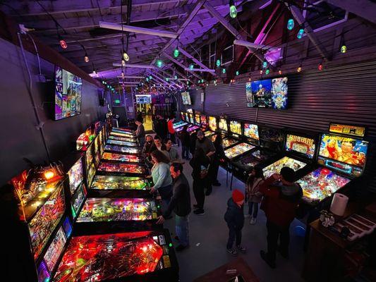 Overhead view of people playing pinball in the evening lighting.