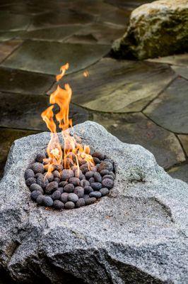 Flagstone compliments verdant woodland plantings. A natural gas, easy-care fire feature is set in a custom hewn granite boulder.