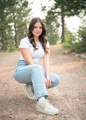 Outdoor Senior girl portrait. sitting on a gravel road casual jeans and white T shirt. Big shoe pose.