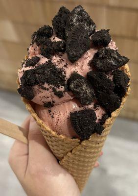 Strawberry ice cream in a waffle cone with oreos as toppings