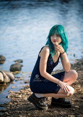 Senior High School Girl outdoor portrait with died colored hair with cute little blue dress Crouching by the creeks edge