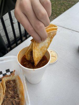 Birria queso taco goes for a dip in the meaty consommé.