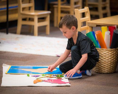 A young student working with a wooden map on the floor.