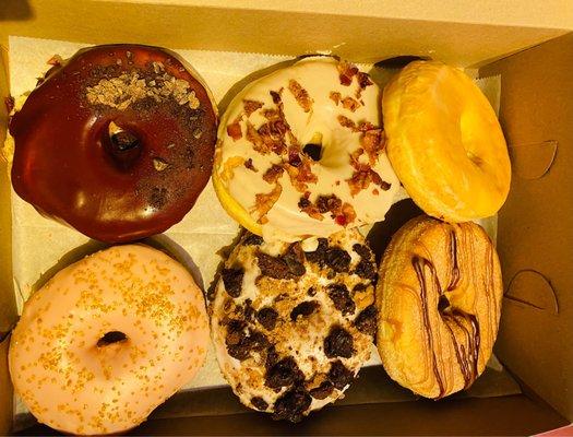 From top left moving clockwise: Chocolate + Cherry, Maple Bacon, Glazed, Churro, Brookie, and Peach Bellini