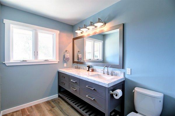 Double sink industrial vanity with carrara marble top paired with an old world industrial vanity light and porcelain tile.