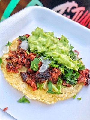 Smoky Pork chorizo taco on a Handmade yellow corn tortilla garnished with a blend of chopped white onions/cilantro topped with guacamole.