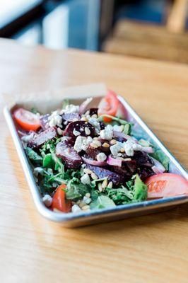 Our Beet Tomato Salad is made with roasted beets, tomatoes & onions, tossed in a citrus-hefeweizen vinaigrette, served on a bed of greens