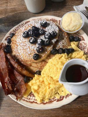 3 Blueberry topped pancakes, with eggs, sausage and bacon. This could easily be shared but this was the serving for one person.