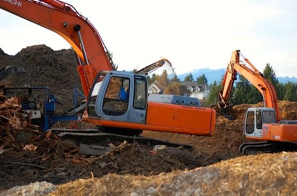 An excavator feeding the grinder where we grind up brush/stumps/yard waste/ and urban wood for recycle.