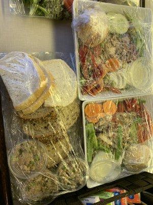 Two salads and a tray of ugly supermarket bread with three small plastic containers of what appears to be tuna salad. Not that you can tell