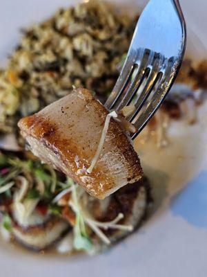 A fork holding a piece of the Pan Seared Scallop on its way to be savored.