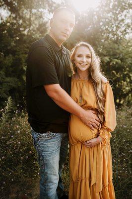 a pregnant mom in a mustard yellow dress with long blonde hair smiles with her hand on her big round belly