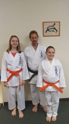 Sensei Bruce Randall, Head Master of Randall School of Karate in Exeter with Maddie and Collin Hardy after they received their Orange belts.