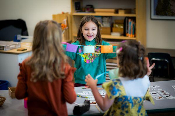 An elementary student happily showing off a colorful paper chain she has made.