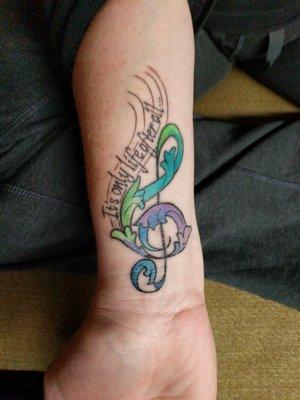 Tattoo number two by Chris. A colorful treble clef with lyrics from an Indigo Girls song.