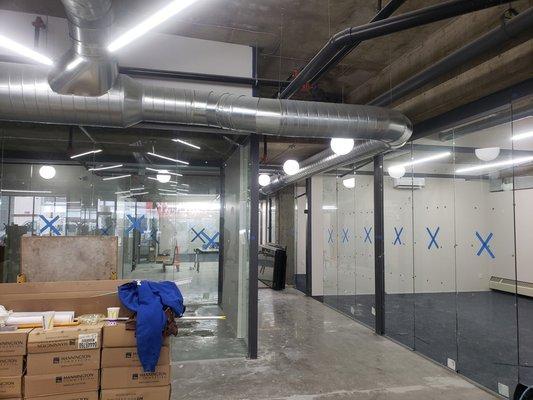 New duct work in a open floor plan office space with hidden refrigeration lines in PVC piping and painted to match existing piping.