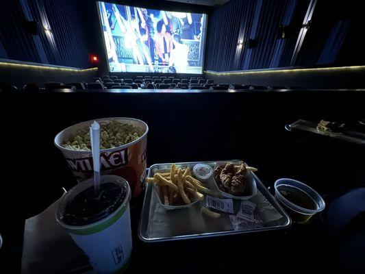 Food on the tray that is attached to the seat. Size of $7 soda and $10 bucket of popcorn.