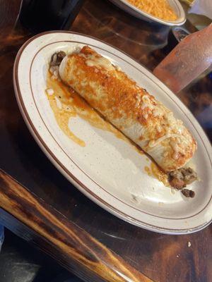 A ground beef burrito with cheese onions tomatoes and sour cream inside