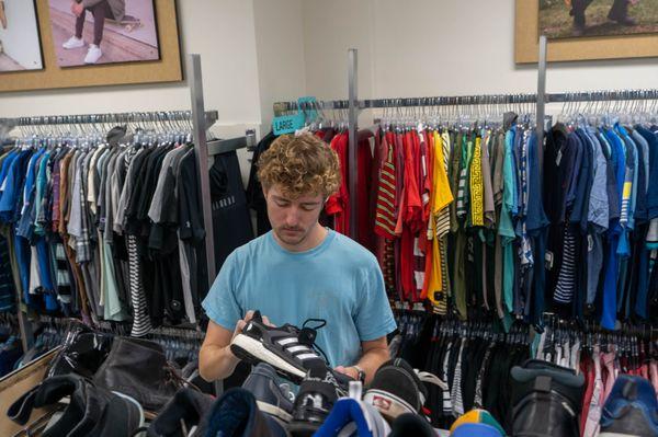 guy with blond curly hair in blue tshirt looking at shoes.