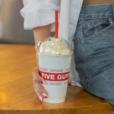 A close-up photograph of a woman holding a Five Guys milkshake.