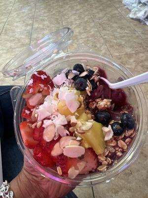 Acai bowl with pineapple strawberries blueberries coconut almond slices and a honey drizzle