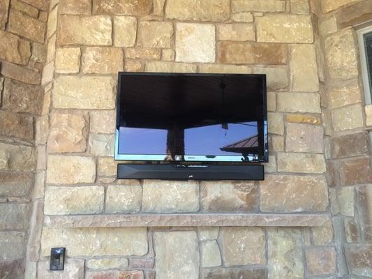 TV and soundbar installed in stone above outdoor fireplace