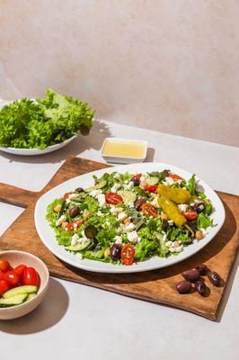 Our Greek Salad is a classic! Baby greens, kalamata olives, tomatoes, cucumbers, feta, pepperoncini, peppers, beans, lemon vinaigrette.