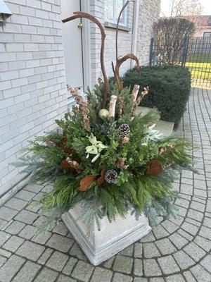 A naturalistic winter arrangement with evergreen boughs, pine cones, birch poles, fantail willow, magnolia leaves, etc.