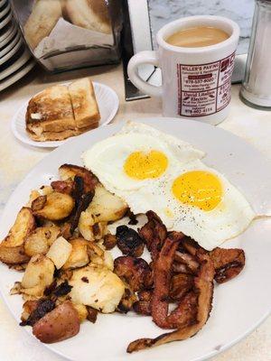 Two eggs sunny side up, crispy home fries and crispy bacon w a side of toast and fresh coffee