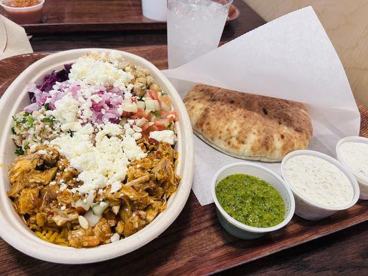 Spicy Chicken Rice Bowl with Pita and garlic sauce, cilantro sauce, and tzatziki on the side.