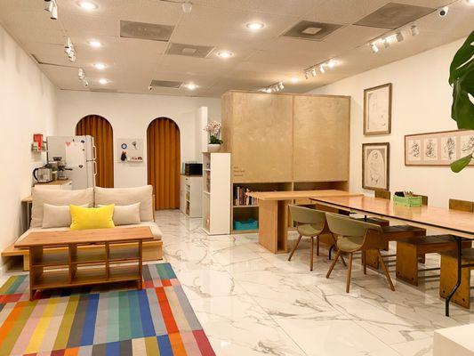 Wide view of our office: couch and coffee table on a colorful rug and our massive work tables.