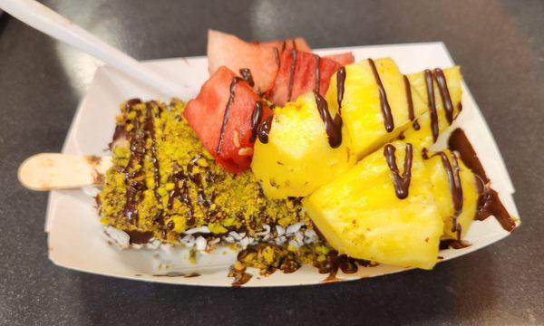 Dark chocolate dipped hazelnut paleta with pistachios, shredded coconut, pineapple and watermelon chunks.