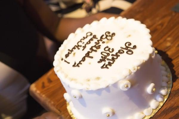 Chocolate cake with strawberry jam layers, covered in white buttercream and decorated with gold sparkle and chocolate lettering.