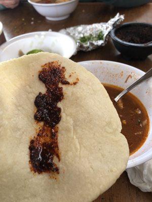 Salsa on tortilla with a bowl of Birria