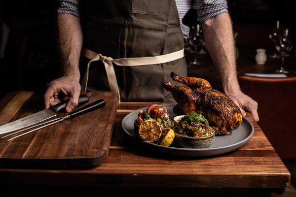 A dramatic wood oven roasted Mary's chicken dripping with flavor, carved at your table