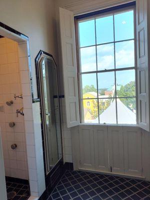 The shower with the side jets and the full length window with built in shutters in the black and white bathroom