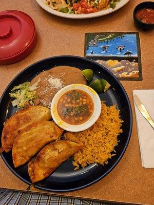 Birria tacos with refried beans and rice and a cup of dipping consomme .