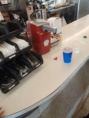 Mess left by the condiments, trash out and on food service counter.