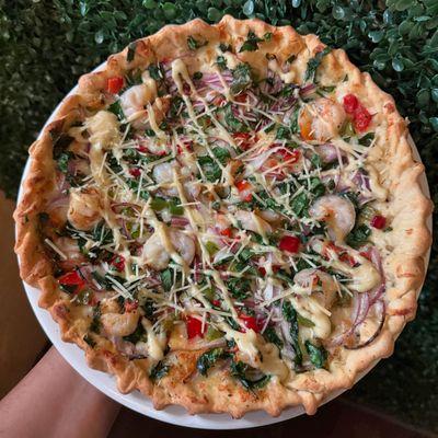 Creamy Cajun sauce Pizza topped with shrimp, onions, bell peppers, and spinach drizzled in Cajun sauce.