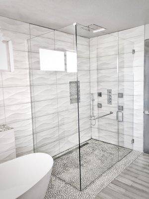 Curbless, frameless glass shower door with a towel bar in the adjacent glass panel installed in Parker, Colorado.