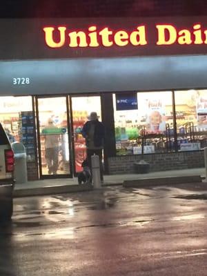 A man ties his dog up at a post at about 10 pm and leaves it to go get his cigarettes. You can tell his priorities.