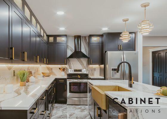 Kitchen in Sterling Heights, Michigan. Black cabinets with gold hardware. Marble countertops and backsplash with hammered sink.