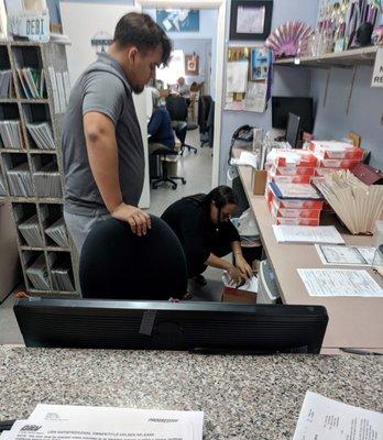 The staff keeps records in no particular order in old cardboard boxes on the floor next to a trash can.