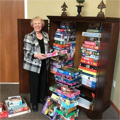 A resident smiling and picking a puzzle from an overflowing activity cabinet.