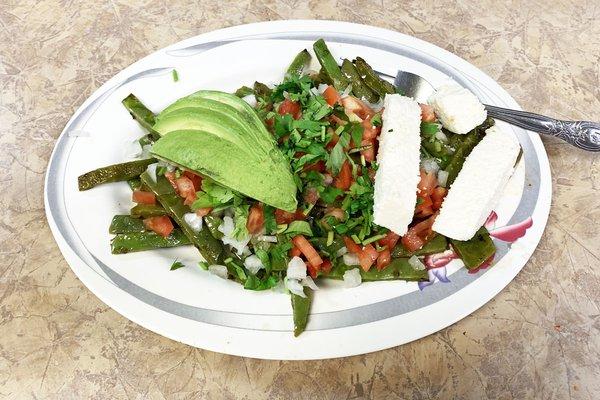 Nopales (cactus) salad with half of a sliced avocado, chopped tomatoes, parsley, and a mild Mexican firm crumbly cheese