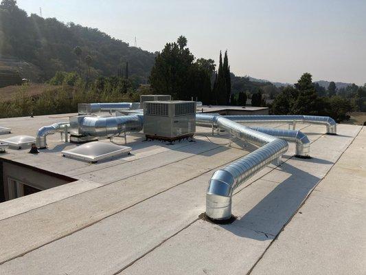 Spiral rooftop ducting and two package units being installed.