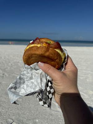 Breakfast sandwich with egg, bacon, avocado, croissant bun.