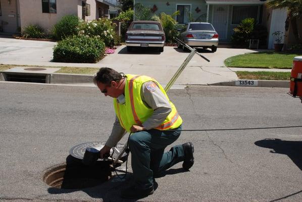 A vector control specialist inspecting a manhole for mosquito breeding